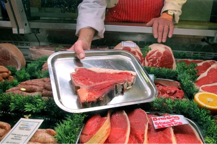 A Churston butcher presenting a T-bone steak over the meat counter